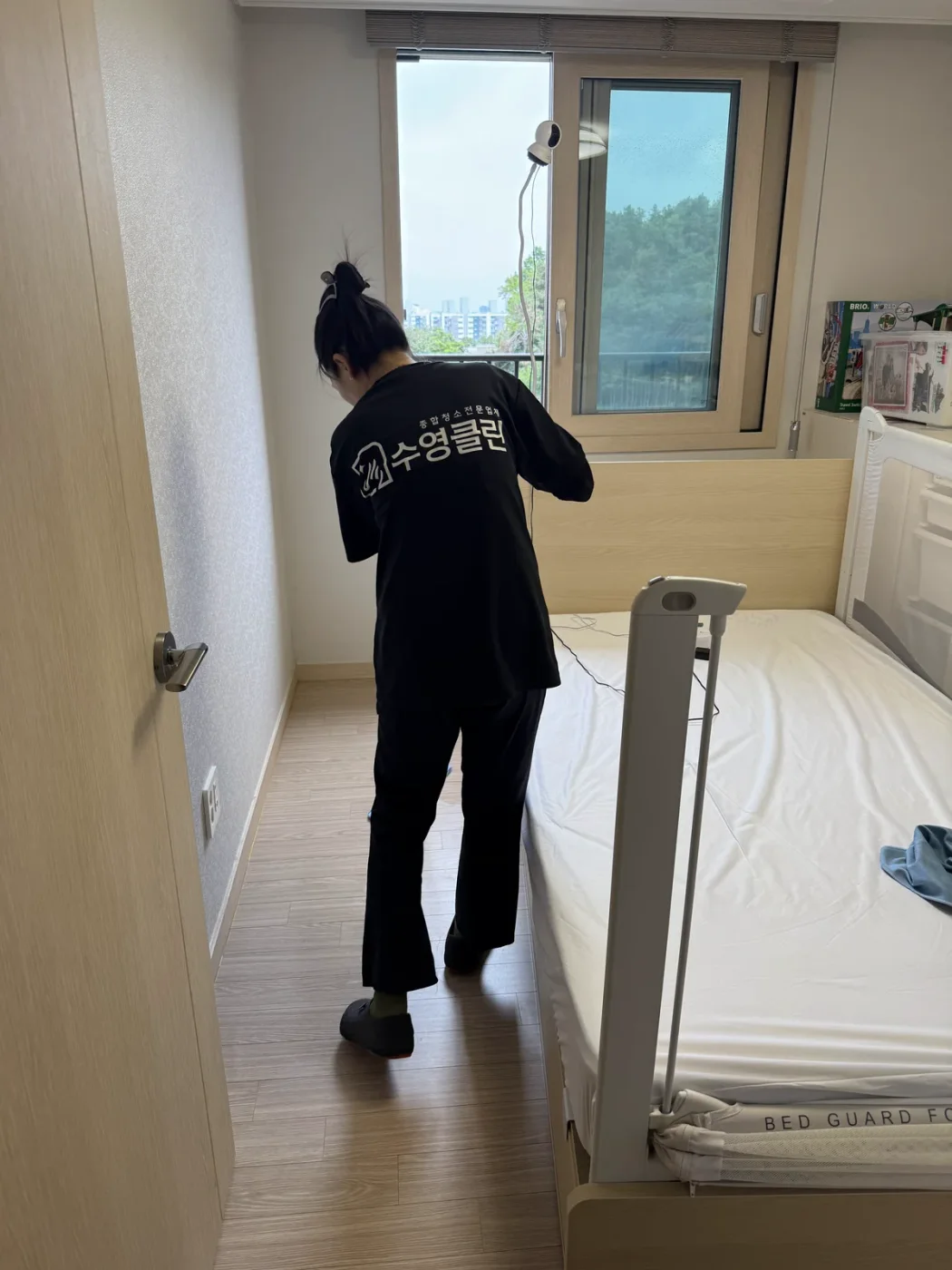 방 안 가구 주변을 정리하며 청소하는 작업자